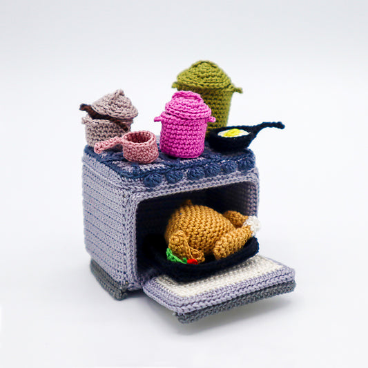Crocheted stove with various pots and a roasted chicken on a white background