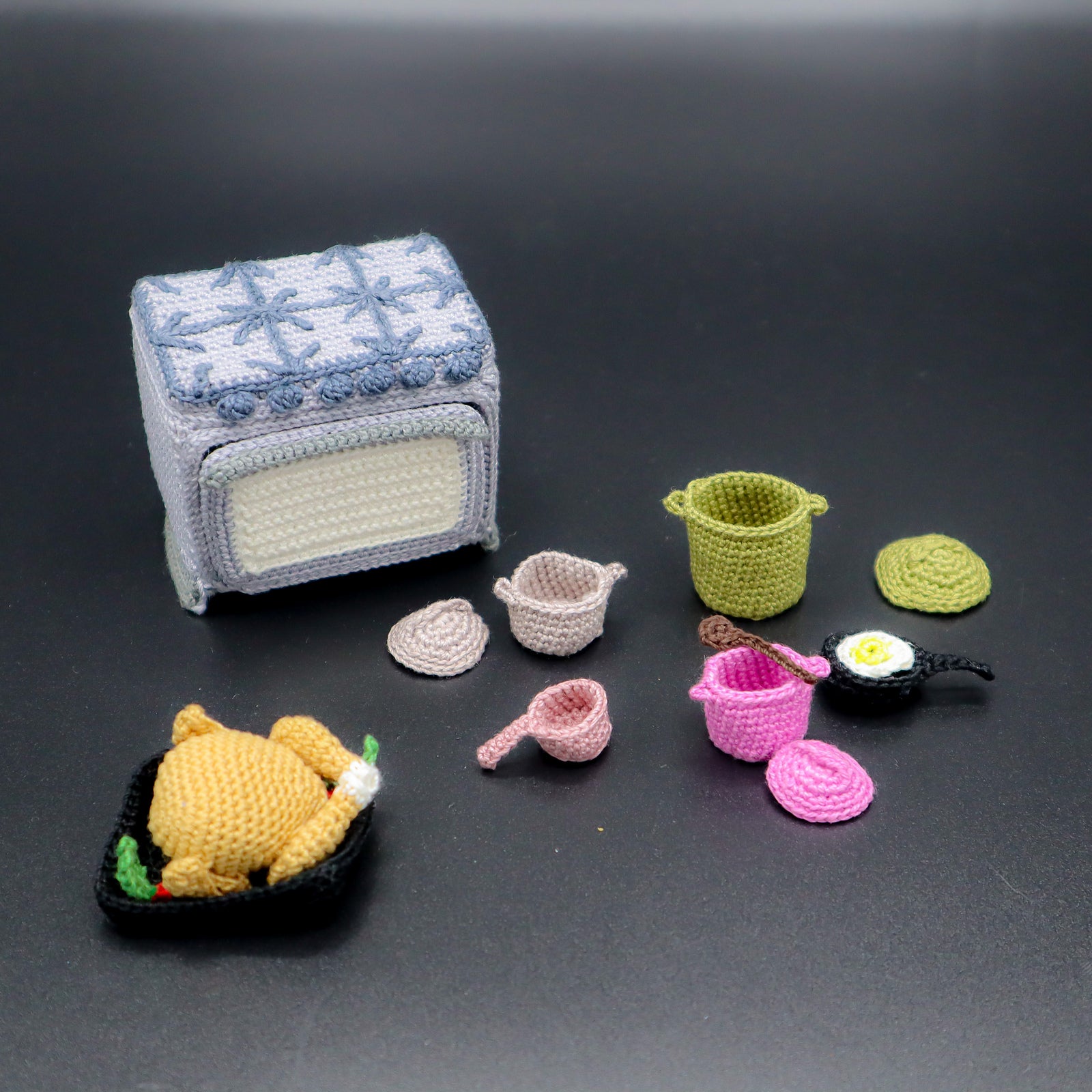Collection of crochet kitchen items including a refrigerator, pots, and food on a dark background